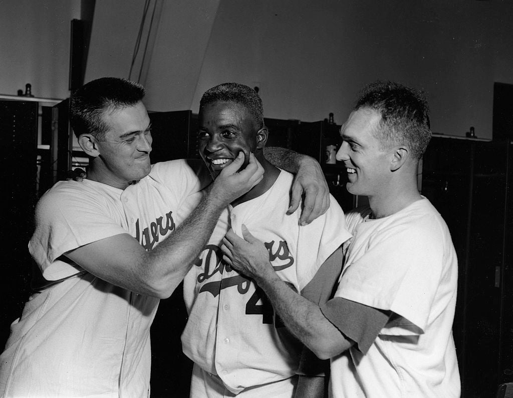 Jackie Robinson, first baseman for the Brooklyn Dodgers, receives pinch on the cheek congratulations from winning pitcher Clem Labine, left, and starting pitcher Carl Erskine, after knocking in all three runs in an August 1, 1948 game vs. Milwaukee Braves at Ebbets Field in Brooklyn. (Photo by Mark Rucker/Transcendental Graphics, Getty Images)